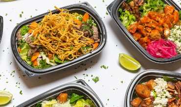 a selection of food in black containers on a white table