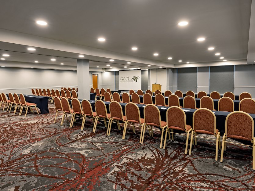 A large conference room with rows of tables and chairs, a podium, and a logo on the wall.