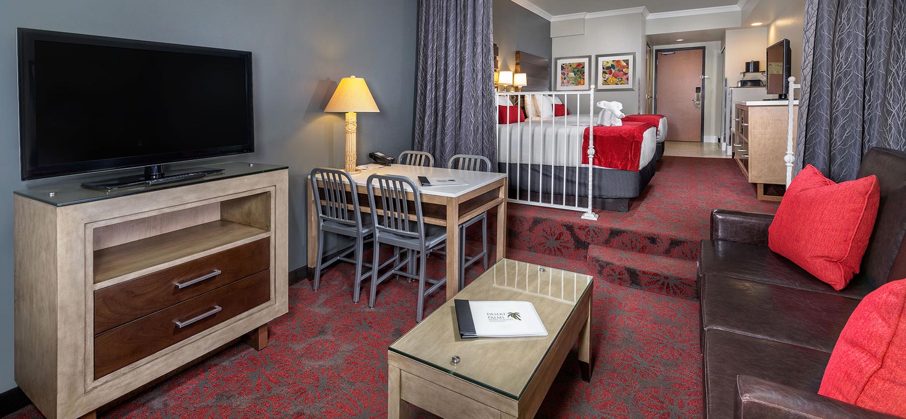 A wide view of a hotel room with a king-size bed, sofa, dining table, and TV.