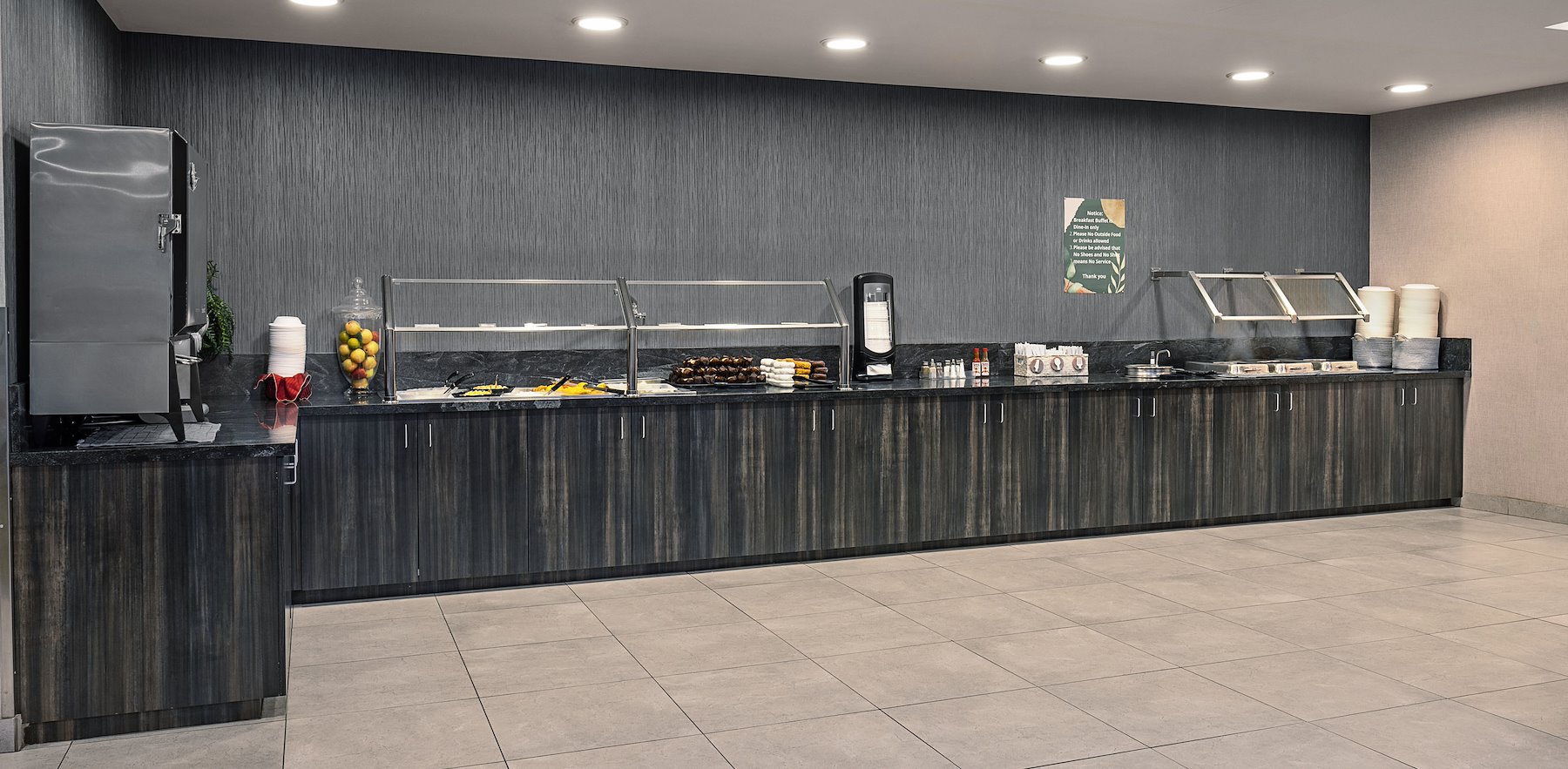 A long buffet counter with food warmers, beverages, and a selection of breakfast items.